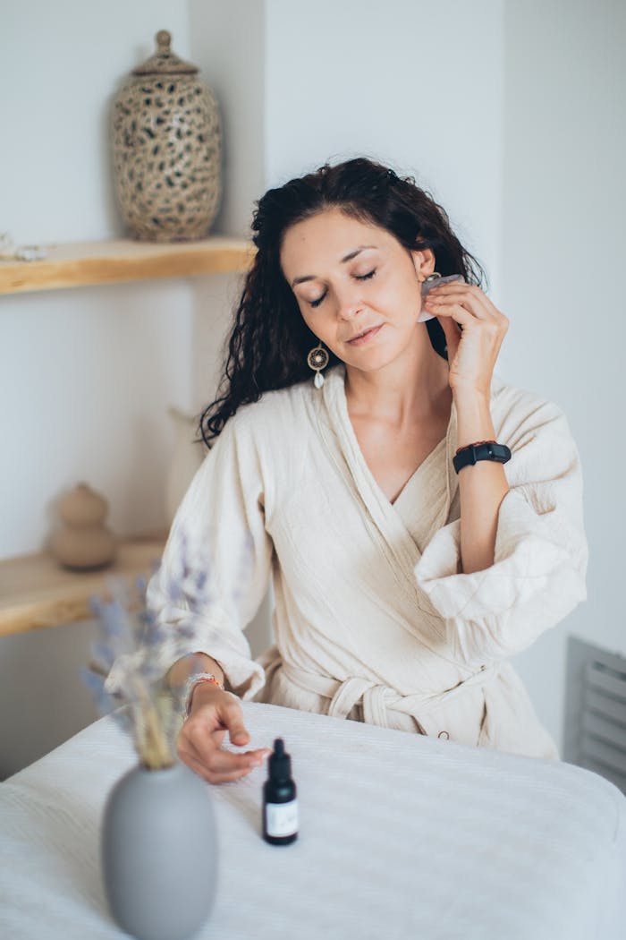 A woman in a bathrobe enjoying a self-care routine with essential oils in a spa-like setting.